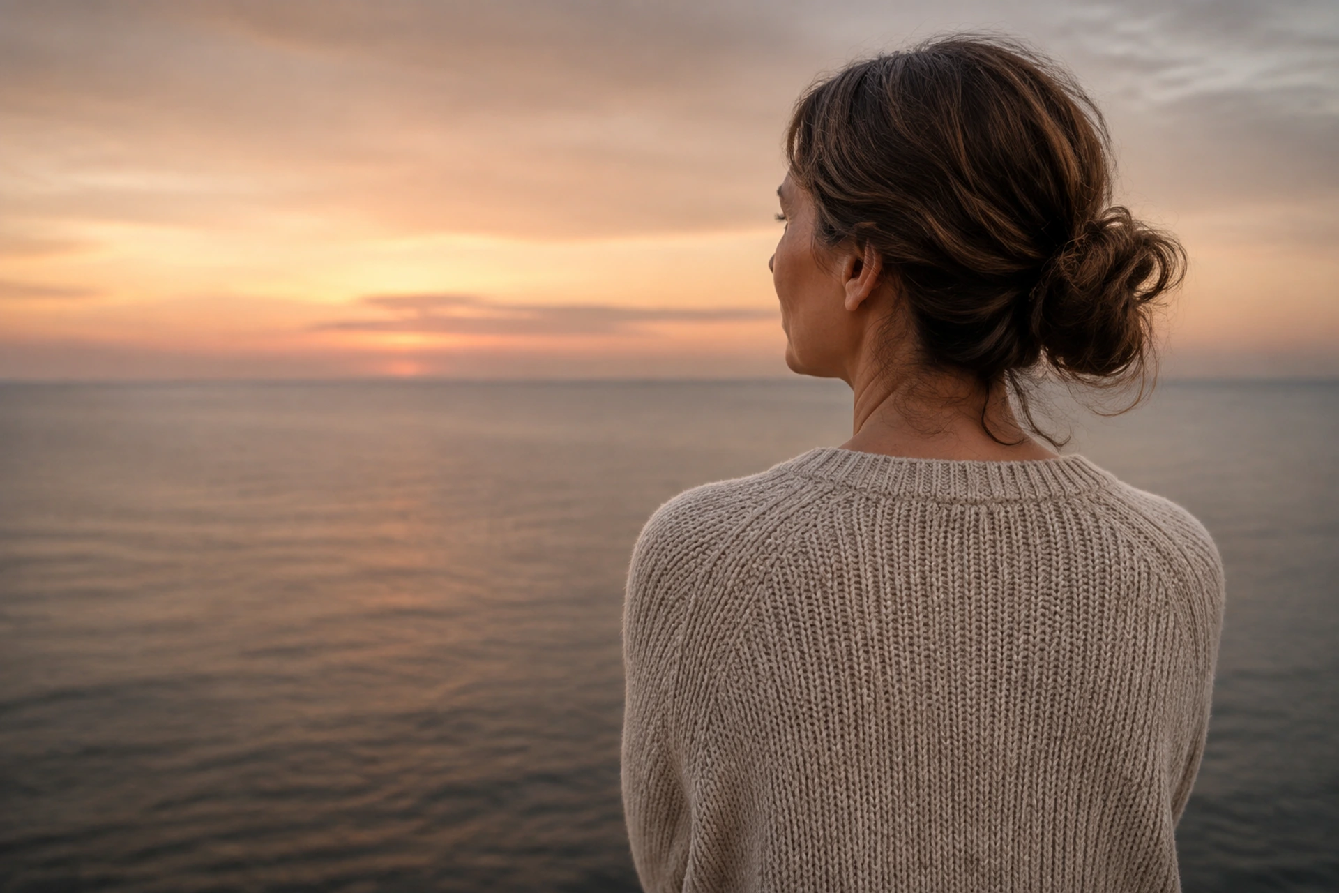Una mujer con un jersey de punto contempla el mar al atardecer.