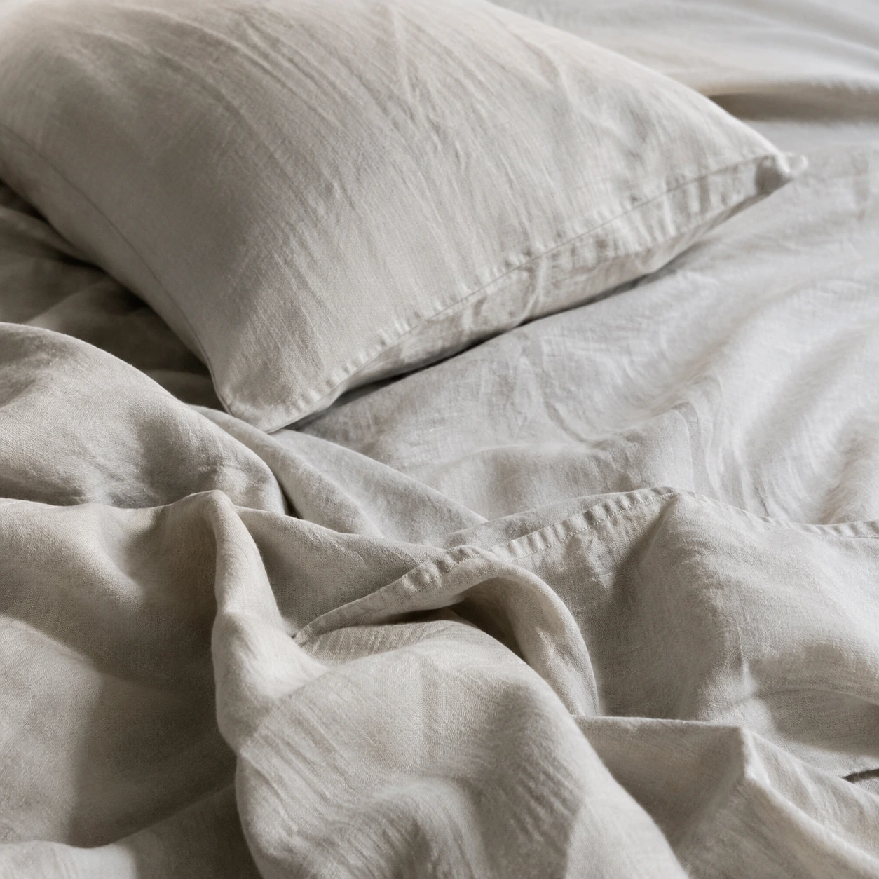 Sábanas de lino y una almohada bajo una luz suave.